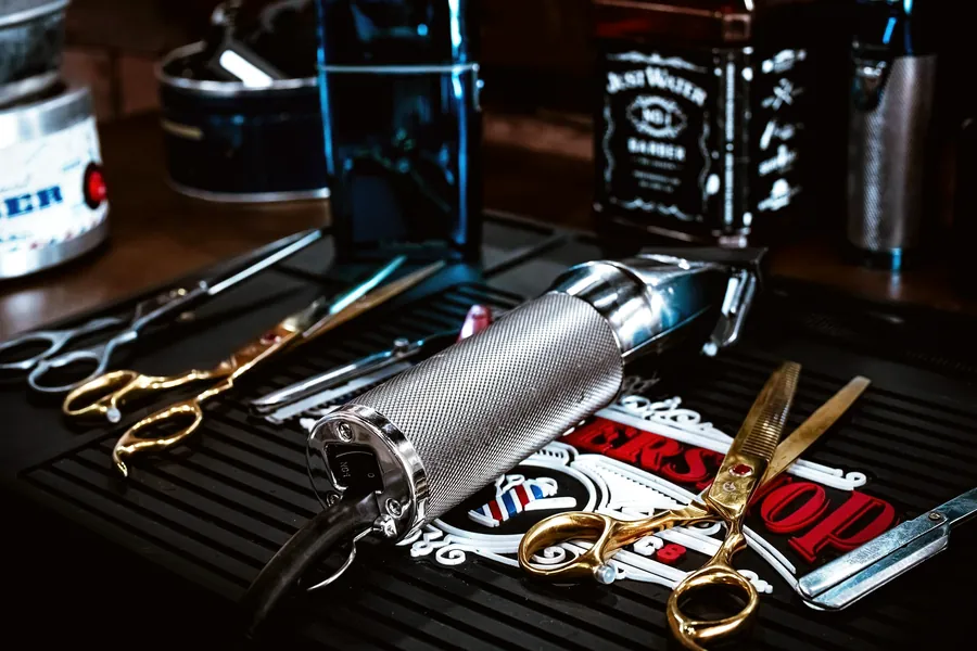 Clippers, shears and a straight razor laid out on a barber station mat.