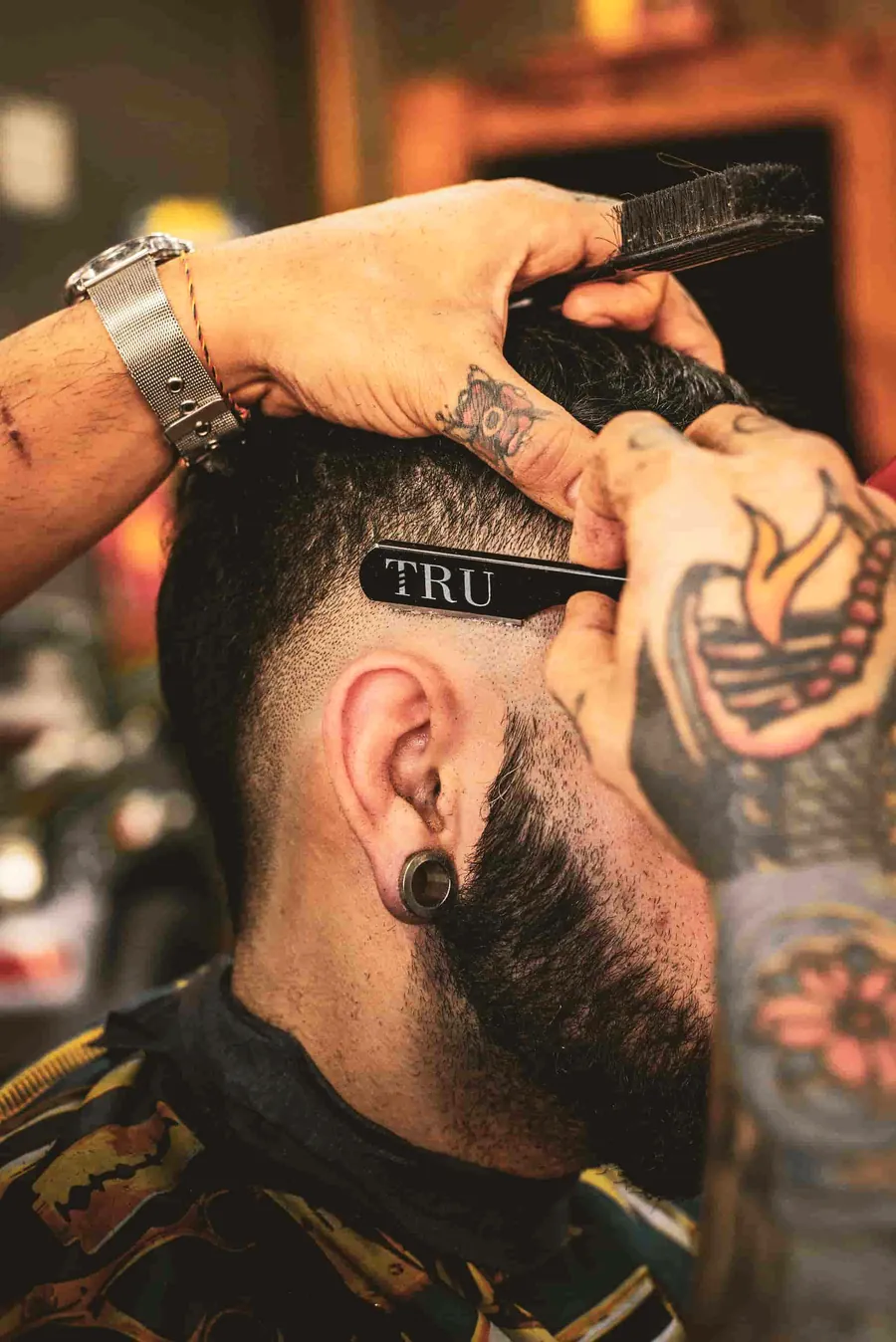 A barber combing through the top of a mid fade on a tattooed client.
